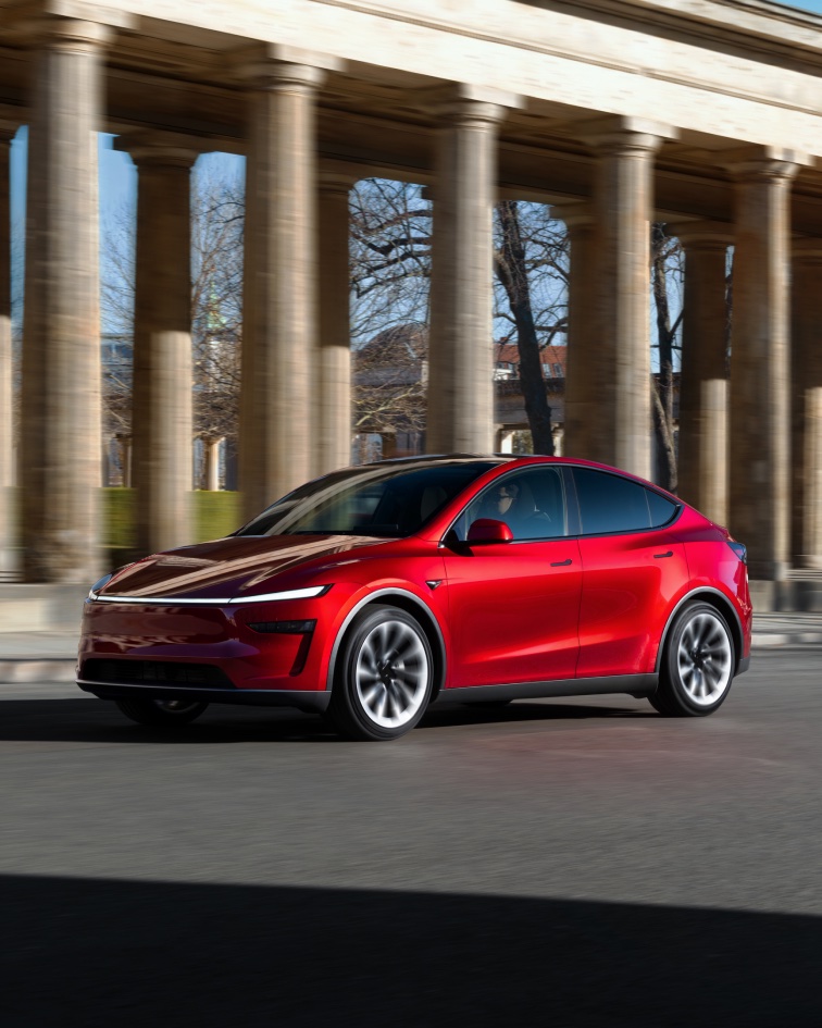 Red Tesla driving past stone columns